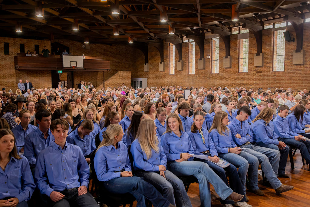 Group of young people in blue shirts and jeans seated in the front row of a large hall