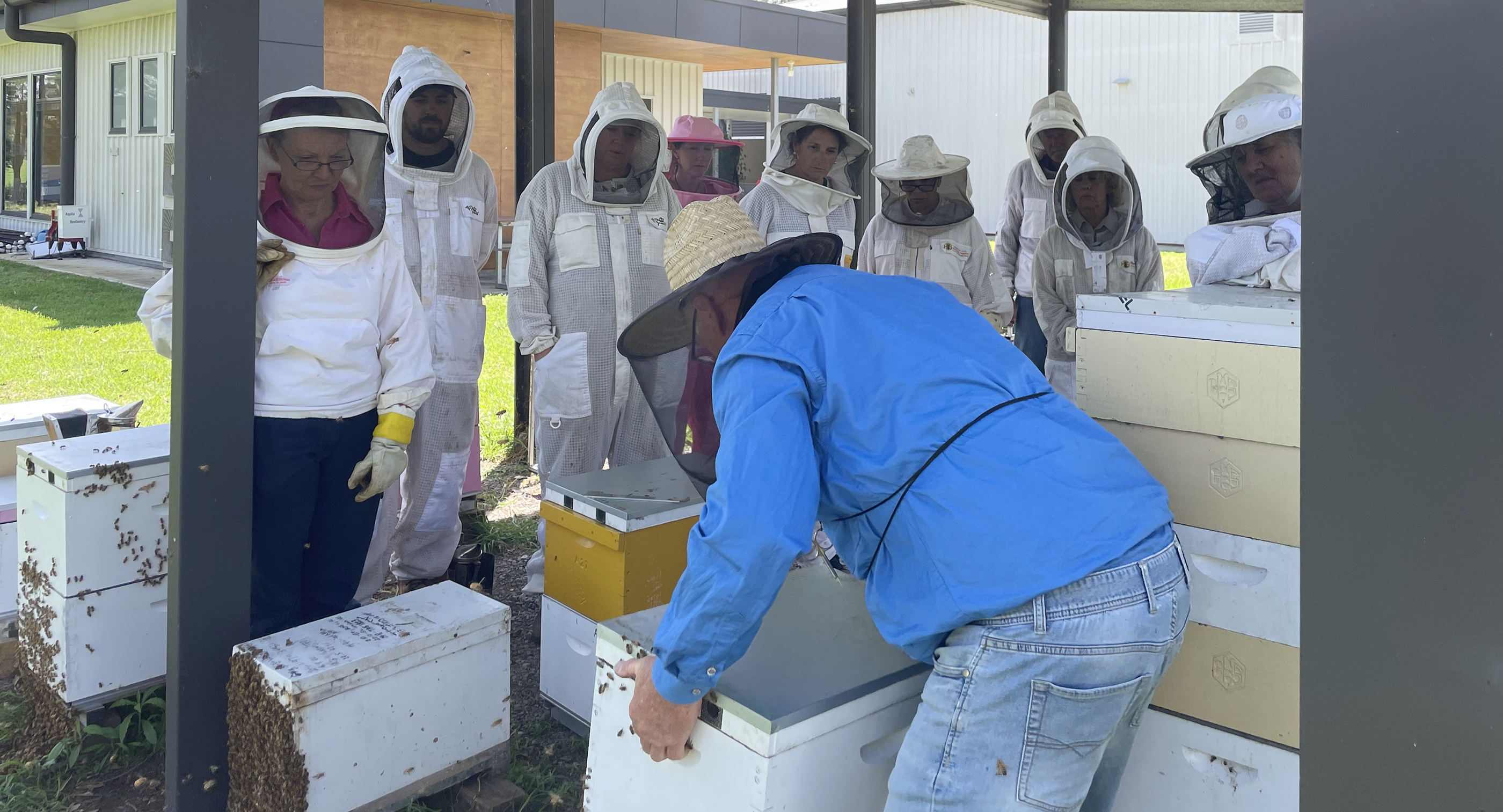 Group of beekeepers watching a trainer open a hive